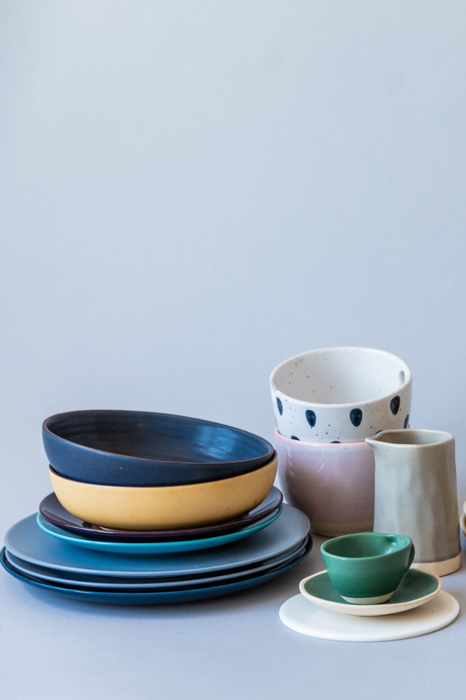 A colorful collection of stacked ceramic plates, bowls, cups, and a pitcher