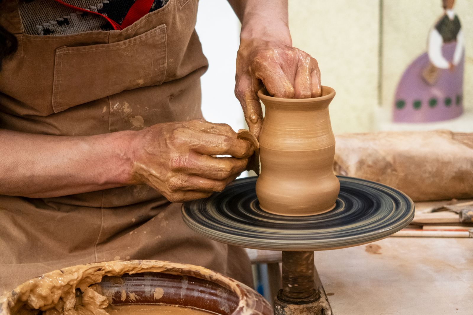 Hands shaping a clay vessel on a pottery wheel